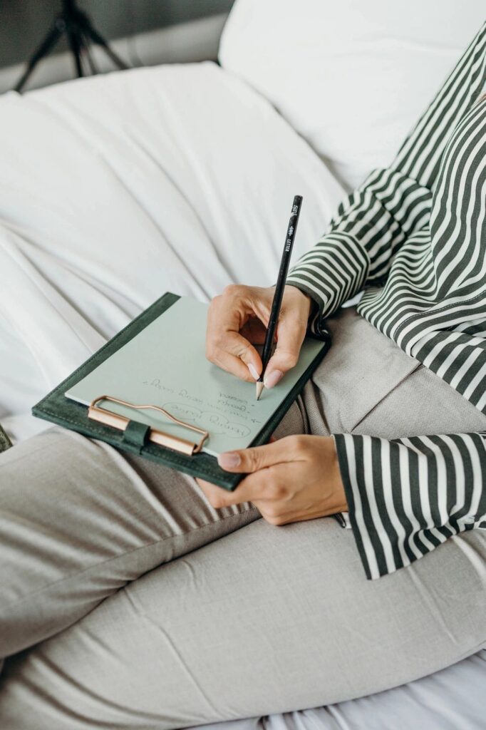 image of person writing with a pencil on a piece of paper attached to a clipboard